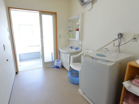 浴室と繋がった脱衣所には洗面台や椅子、洗濯機、棚などが並んでいる。またナースコールも設置されている。