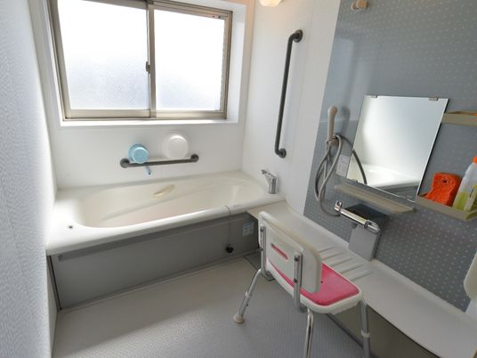 転倒防止の手摺りが随所に設けられた清潔な浴室。洗い場には使いやすいよう棚や肘掛のついた椅子が用意されている。