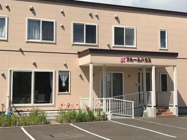 アヤメが彩るエントランス 外観 ゆったりしたアプローチをもつ建物前には、美しいアヤメが咲き誇っています。窓越しには、快適な空間で過ごす方の姿が見え、温かな雰囲気を感じることができます。