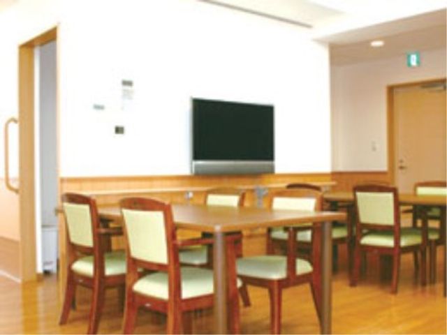 共有ダイニングルーム 食堂 木製のテーブルと椅子が配置された食堂で、壁掛けの大型テレビが設置されています。明るい雰囲気の中、食事を楽しむことができる空間です。