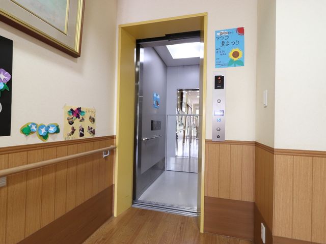 清潔な廊下のエレベーター エレベーター 廊下はハンドレールが整備されており、壁には掲示物が飾られています。利用者が安心して移動できる工夫がされた空間です。