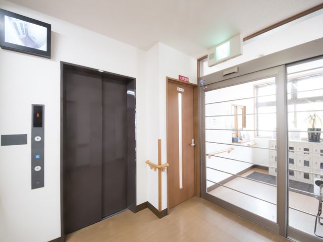 明朗な雰囲気のエレベーターホール エレベーター 広々としたエレベーターホールは、自動扉が設けられ、明るく清潔な雰囲気です。入口には待合スペースも備え、利便性を重視した設計になっています。