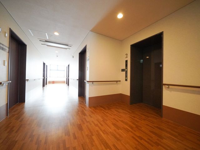 快適な廊下の風景 廊下 床には木のぬくもりを感じさせる素材が使われ、手すりがしっかり取り付けられています。明るく清潔感のあるこの通路は、皆様が日々快適に過ごせる環境を提供しています。