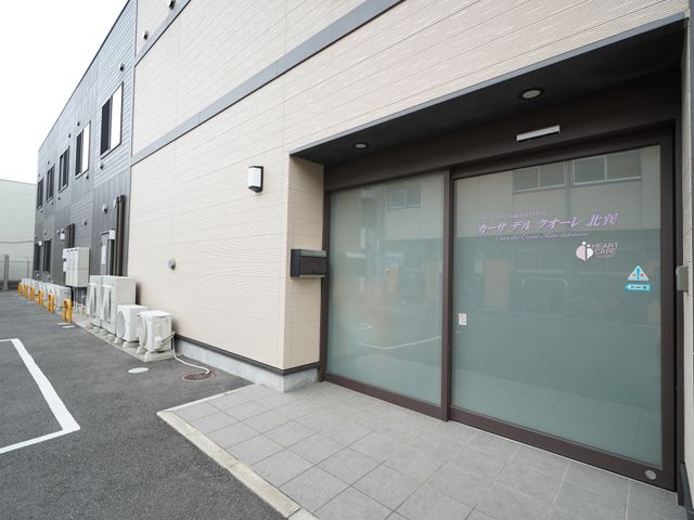 施設の外観とエントランス 入口 暖かい色合いのエントランスは、やわらかな印象を与え、来訪者を穏やかに迎え入れます。明るい日差しの中、お仕事に向けての一歩を踏み出しませんか。