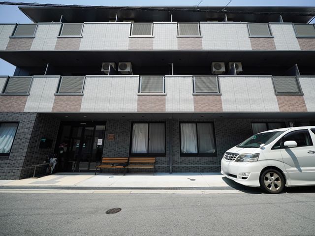 建物前のベンチと車 外観 ゆったりとしたベンチが設置されたエントランスは、来訪者を温かく迎え入れる造りとなっており、待ち合わせにも便利です。