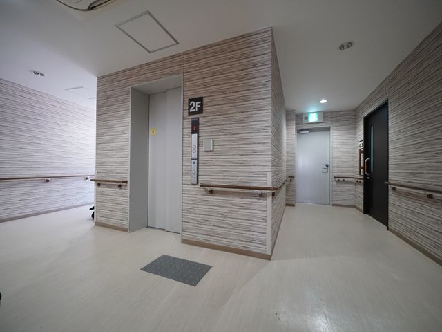 白基調の清潔な廊下 エレベーター ゆとりある通路が確保された清潔感のあふれるスペースです。壁に手すりが取り付けられ、どなたでも安全に移動できる環境が整っています。