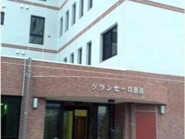 白い建物のエントランス 外観 落ち着いた色合いの入り口が迎える、清潔感のある建物です。この門をくぐると、新たな職場での一歩が始まります。