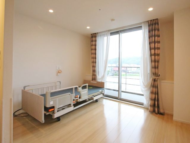 明るい洋室と窓のカーテン 居室 広々とした居室には、必要な設備が整えられ、大きな窓から自然光が差し込んでいます。ゆったりとした時間をお過ごしいただける空間です。