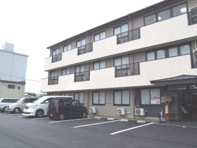 明るい外観の施設エントランス 外観 広々とした駐車スペースがあり、入り口には花が飾られています。利用者の方々の安全と快適な来訪を支える環境が整っています。