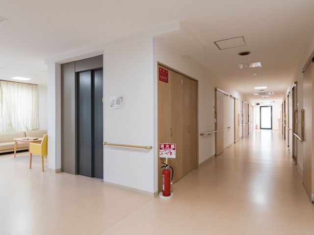 明るい廊下と開いたエレベーター 通路 やわらかな光が差し込む広々とした廊下は、行き来する際にも安心です。手すりや消火器が設置され、安全に配慮された環境が整っています。