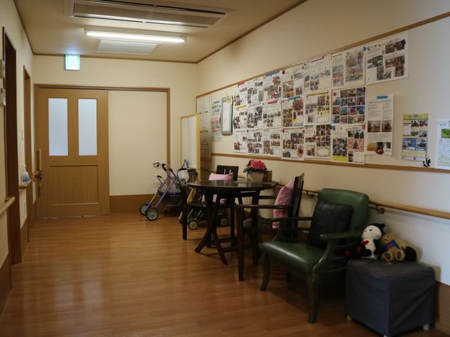 暖かみのある休憩室 掲示板 木目調の床とやわらかい照明が落ち着いた雰囲気の休憩スペースです。壁には活動の様子が写った掲示物があり、見るだけで暖かい気持ちになります。
