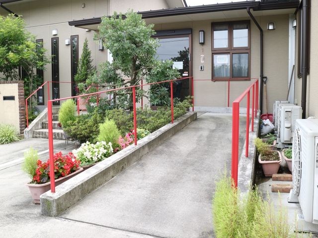 花と緑のあるエントランス スロープ 手すりが設置されたエントランスは、花々と緑に囲まれており、安全かつ穏やかな出入りが期待できます。