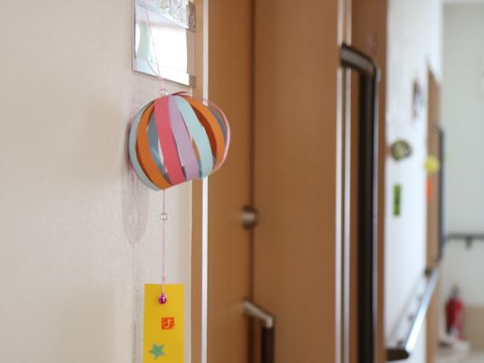 さまざまな色画用紙を使用し、風鈴に見立てた作品が居室扉横のネームプレートに紐に吊るされ掛けられている。