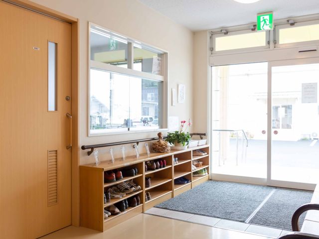 明るいエントランスの様子 玄関 きれいで開放的な受付エリアが迎えてくれます。来訪者の印象も温かく、訪れた人々を心地よくさせる工夫が感じられます。