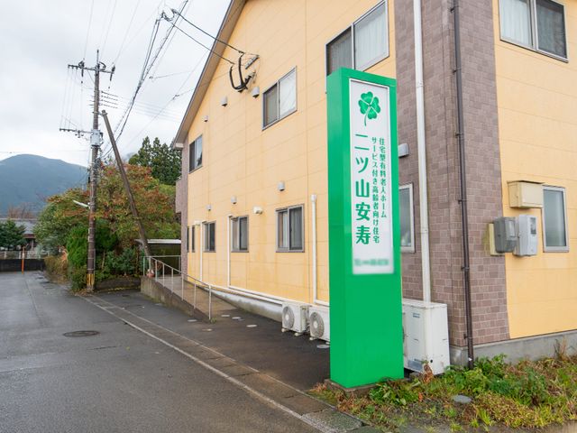 黄色い建物と緑の看板 外観 明るい黄色の外壁が印象的な施設です。緑の看板が目印となり、安心してご訪問いただけます。