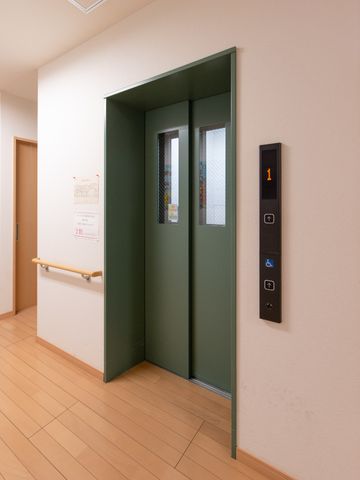 緑色のエレベーター扉 エレベーター 手すり付きで安心のエレベーターです。移動の利便性を考慮した設計で、皆様の快適な生活をサポートいたします。