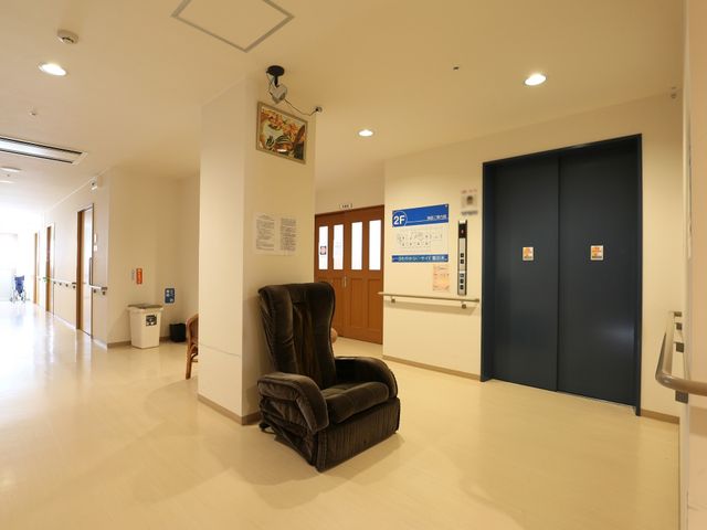 廊下にある快適な椅子 エレベーター 明るく広々とした廊下は、ゆったりとした一人掛けの椅子が配置され、一息つくことができる落ち着いた空間を提供しています。