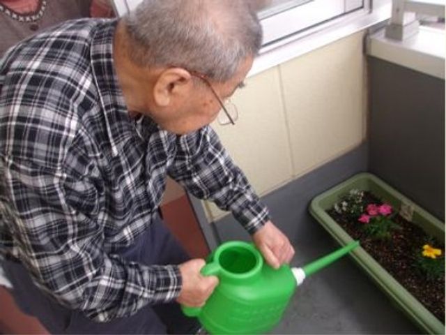 お花に水をやる高齢者 日常 バルコニーで植物のお世話を楽しむ姿が見られます。日々の生活に彩りを添える趣味活動が充実しています。