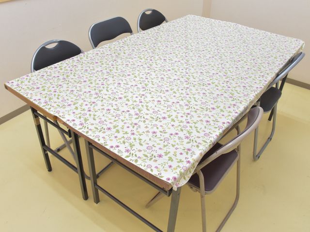 花柄のテーブルクロスが敷かれたテーブル 談話スペース 明るく清潔感のある食事スペースで、花柄のテーブルクロスが温かい雰囲気を演出しています。働くあなたにもリラックスできる空間が広がっています。