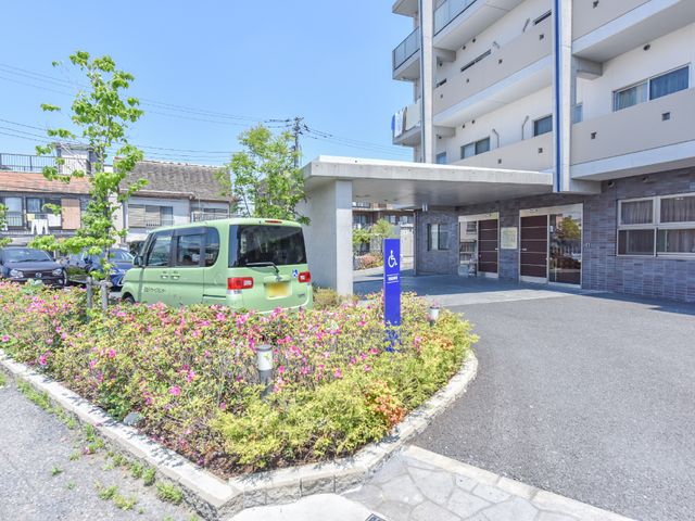 花壇とエントランスの景色 外観 ゆったりとしたスペースのあるエントランスは、来訪者を温かく迎え入れます。植栽が施され、明るく開放的な雰囲気を演出しています。