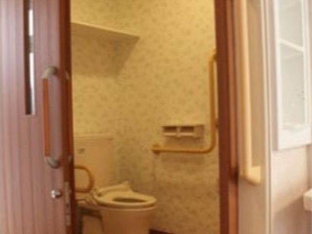 居室の扉とトイレ 共有トイレ ゆとりあるスペースの清潔なトイレです。手すりが設置されており、安全にご使用いただけます。