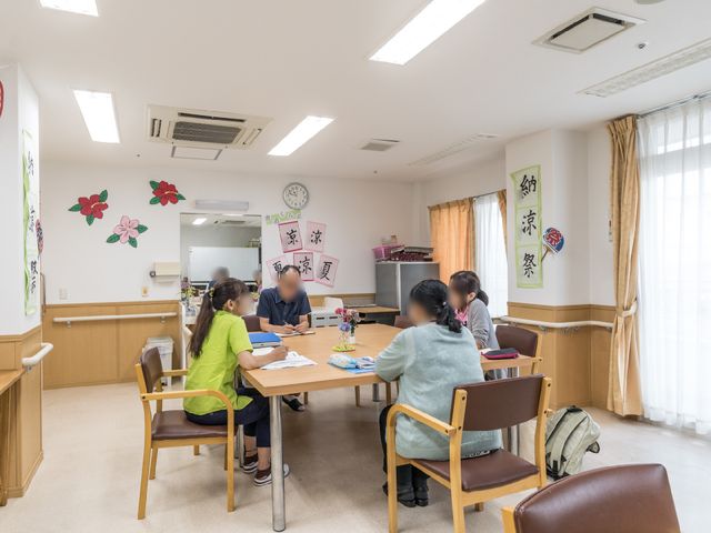 共有スペースの活動風景 共有スペース ゆとりのある多目的室で、利用者のみなさまが穏やかな時を過ごされています。壁に飾られた彩り鮮やかな装飾が、温かい雰囲気を演出しています。