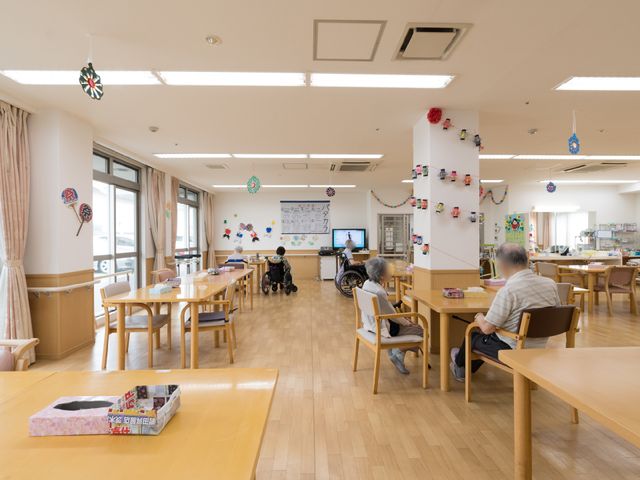共有スペースの様子 ダイニング 広々とした食堂で、利用者がくつろいでいます。木目調のテーブルと優しい光が心地良い空間を演出しており、日々のコミュニケーションの場となっています。