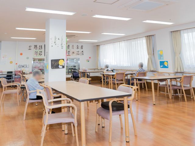 広々とした明るい食堂 コミュニティリビング ゆったりとした椅子が並ぶ食堂で、利用者の方々が自由な時間をお過ごしになっています。日差しの優しい窓辺で、心地よさそうに食事や休憩ができる空間です。