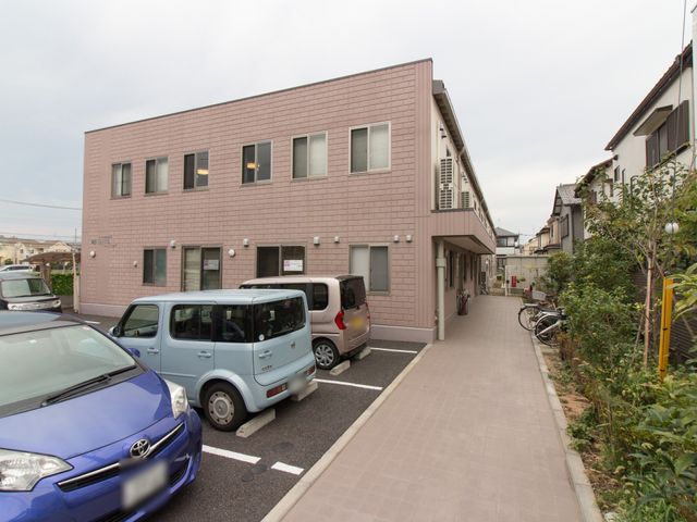 ピンクの外壁の外観 外観 駐車スペースが整備され、落ち着いた色合いの建物が周囲に調和しています。ゆったりとした通路もご利用者の快適な移動を支えています。