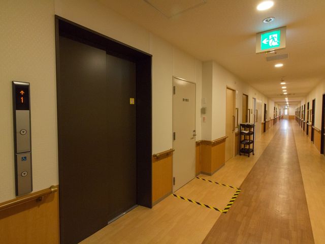 清潔感のある廊下の様子 エレベーター 広々とした通路は清掃が行き届いており、快適にご利用いただける設計です。小物が置かれた台も整然と配置され、居心地の良さを感じさせます。