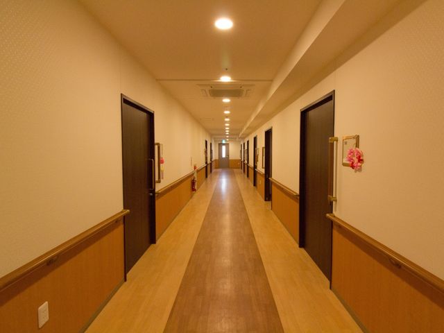 清潔な廊下 通路 明るい色合いの木目調で心地よい廊下は、ゆったりとした幅広設計です。壁に飾られた花がアクセントになり、歩くたびに心が和みます。