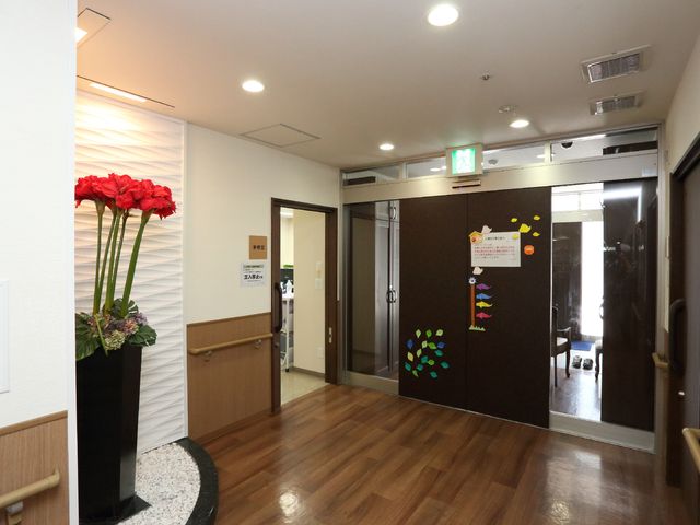 明るい廊下の入口 エントランス 安らぎと清潔感を感じさせるエントランスです。手に花を持つ模様が描かれた壁が暖かい雰囲気を醸し出しています。