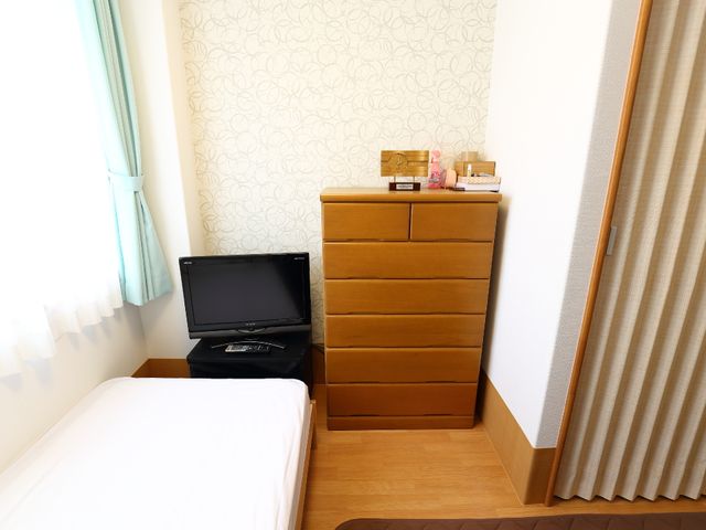 居室の整ったコーナー ベッドルーム 清潔感ある居室には、必要十分な家具が配備され、ゆったりした一人暮らしをサポートしています。窓際の明るさがリラックスした時間を提供します。