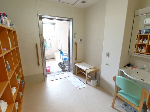 清潔感ある浴室の扉 脱衣場 ゆとりのある入口と清潔な空間が特徴の浴室です。利用者の安全と快適さを考えた設計がされており、就業にあたってはそうした細かな配慮を学べる環境があります。