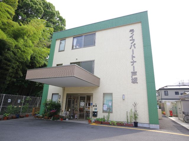 緑豊かな外観の建物 施設外観、前面 植栽に囲まれた温かみのある外観です。明るい雰囲気の入口には観葉植物が添えられ、訪れる方々をやさしくお迎えします。