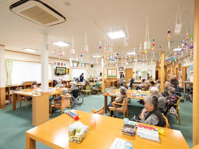 明るい広々とした食堂 食堂 広々とした食堂では、利用者が様々なアクティビティを楽しんでいます。色とりどりの吊るし飾りが温かい雰囲気を創出しており、交流の場を提供しています。