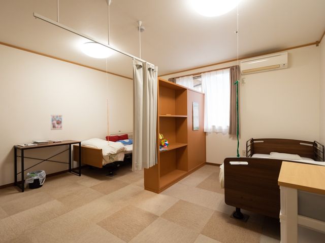 清潔な居室の様子 居室 広々とした居室は、機能的な家具が整い、快適な日常生活を支えます。個々のニーズに合わせたベッドやデスクが配置されています。