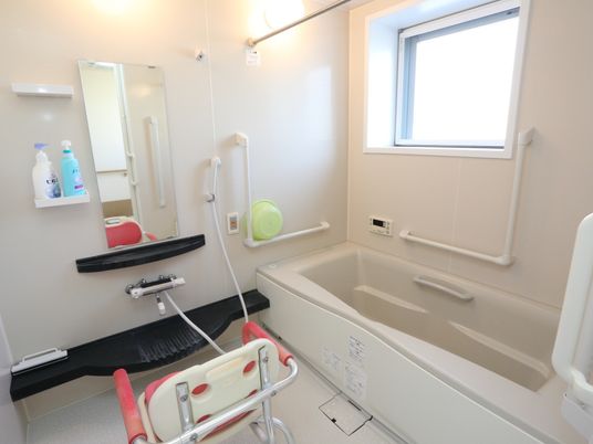 施設の写真 共用の一般浴室。室内は全体が樹脂製になっている。カラン前にある黒い棚は水たまり防止の溝が彫られたデザインになっている。