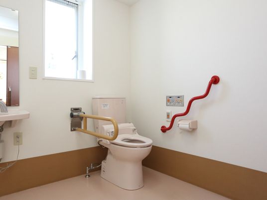 施設の写真 室内に介助者用のスペースが確保された、広い共用トイレ。温水洗浄便座になっており、壁にコントローラーが取り付けてある。