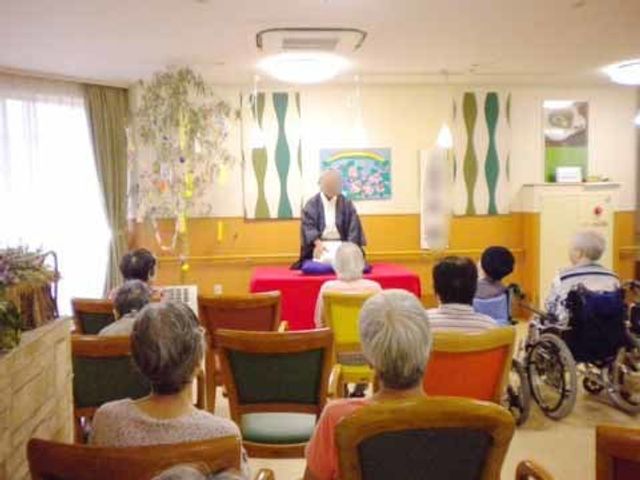 催しを聴く利用者達の様子 イベント 温かみのある多目的室で、集まった利用者が様々な催しに耳を傾けています。皆さまの参加をお待ちしております。