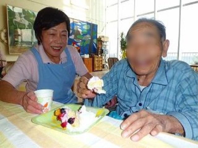 笑顔で手伝う介護スタッフ 日常 明るく広々とした食事のスペースで、笑顔のスタッフがお手伝いしています。利用者の方々が日々楽しいひとときを過ごされています。