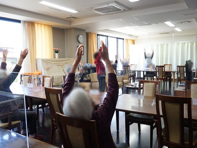 健康体操を行う居室 共有スペース ゆったりとした居室で、利用者の皆さんが健康体操を楽しそうにされています。明るく開放的な空間でのレクリエーションは、日々の豊かな暮らしを支える一環です。