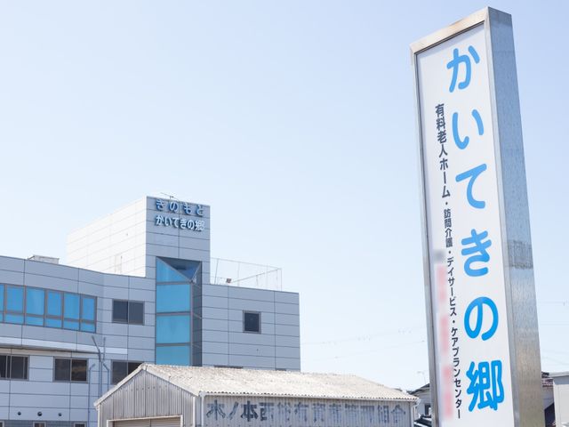 青空背景の建物と看板 看板 清潔感あふれるモダンな外観で、心地よい環境がお迎えします。皆さんのご参加、心よりお待ちしております。