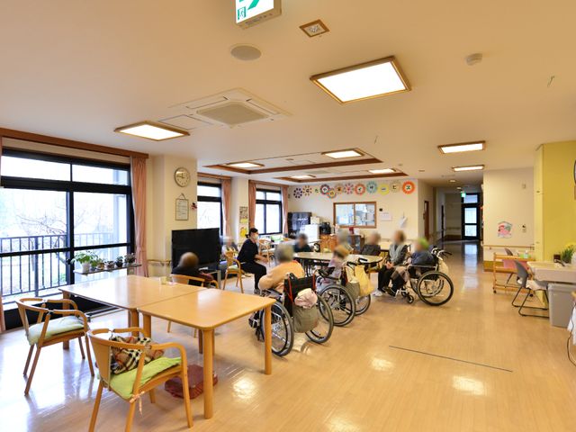 居室で過ごす人々 共有ルームの様子 明るく開放感のある食堂で、利用者の方々がくつろいでいます。合わせて、広々としたスペースでのお仕事が期待できそうです。