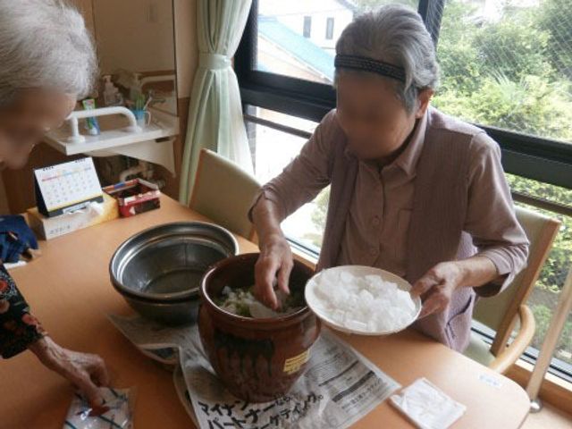 手作業活動する高齢者 梅干し作り 共有スペースで行われる手作業は、日々の活動への意欲を促します。お互い協力しながら、様々な作業を楽しむ姿が見受けられます。