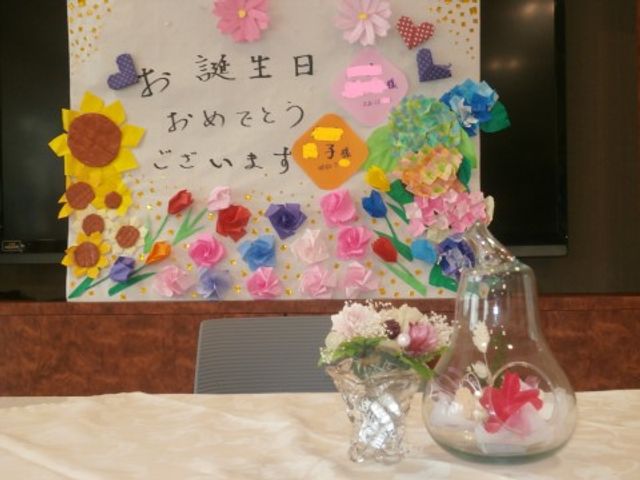 花と掲示物の装飾 誕生会2 手作りの花が飾られた壁面は、温もりと季節感を感じさせる空間です。お食事の時間も豊かな気持ちでお過ごしいただけます。