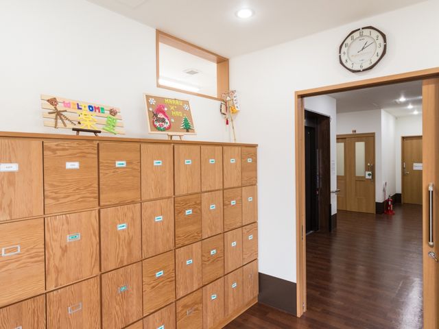 廊下の木製ロッカー 玄関 木目調のロッカーが並ぶ、清潔感のあふれる通路です。壁掛けの時計下では、季節感ある手作りの飾りがほほえましい雰囲気を演出しています。