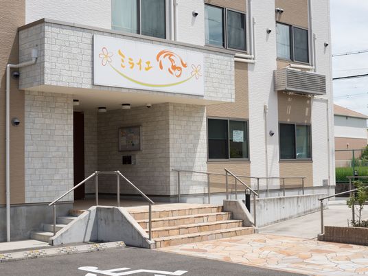 日当たりの良い正面玄関である。看板が正面に設置されている。階段が正面と駐車場側にあり、反対側に緩やかなスロープが設けられている。