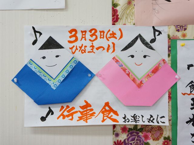 ひな祭りの壁掛け装飾 掲示 ひな祭りを祝して手作りの壁掛けが飾られており、工夫を凝らした楽しい活動が行われていることが伺えます。明るい雰囲気で日々が彩られる場所です。