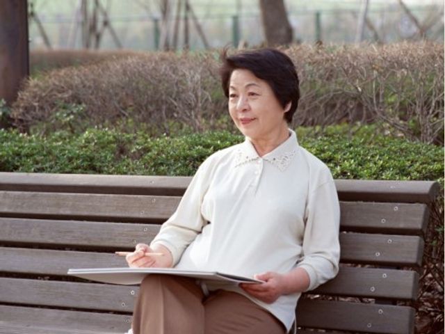 ベンチに座る女性 外出 ゆったりとした中庭で、心地よい自然の中でリラックスして過ごす姿が描かれています。静かな環境で読書をお楽しみの方もいらっしゃいます。